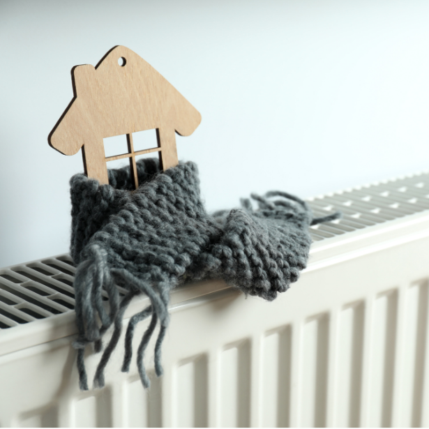 Holzhaus-Schild mit Fenster und grauem, gestricktem Schal auf einem Heizkörper.